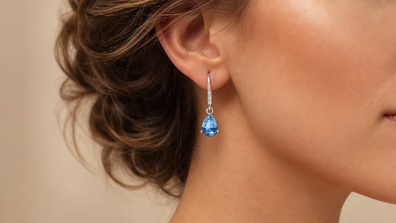 Silver drop earring with blue teardrop crystal worn on an ear